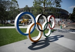 FILE - Construction workers and passersby are seen through Olympic rings in front of the construction site of the New National Stadium, the main stadium of Tokyo 2020 Olympics and Paralympics, in Tokyo, Japan, June 13, 2019.