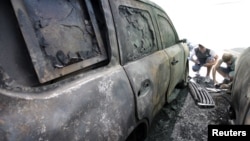 Men take photos of a car belonging to the Organization for Security and Cooperation in Europe (OSCE), which was burnt overnight, near its office in Donetsk, Ukraine, Aug. 9, 2015. 