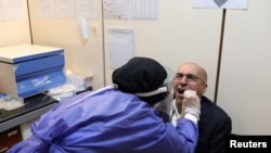 A member of the medical team wears a protective suit as she collects saliva of a man to be checked at a testing center for coronavirus disease (COVID-19), in Tehran, Iran, May 20, 2020.