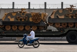 A motorist drives past a Turkish forces truck transporting armored personnel carriers at the border with Syria in Karkamis, Gaziantep province, southeastern Turkey, Oct. 15, 2019.