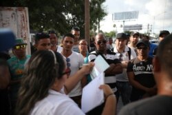FILE - Migrants listen as a Mexican migration officer verifies their identity on a list Matamoros, Mexico, at the foot of the Puerta Mexico bridge that crosses into Brownsville, Texas, Aug. 2, 2019.
