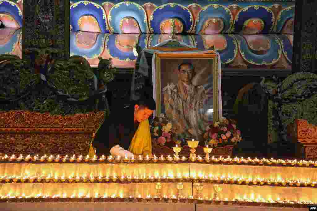 Raja Bhutan Jigme Khesar di ibukota Thimphu menyalakan lilin di dekat foto Raja Thailand Bhumibol Adulyadej yang baru meninggal di Bangkok.