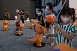 FILE - Children wearing masks to protect from the coronavirus gather near mascots for Guagualong online app for children language learning during a promotion in Beijing, Aug. 21, 2020.