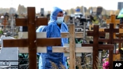 A grave digger wearing a protective suit stands during a a COVID-19 victim burial at a cemetery outside in Omsk, Russia, Oct. 7, 2021.