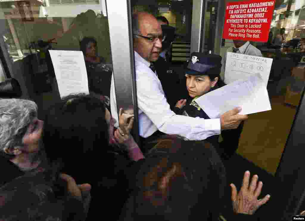 A Laiki Bank manager helps a police officer enter the bank after getting past depositors waiting outside the bank's branch in Nicosia, Cyprus, March 28, 2013.