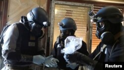 FILE - A U.N. chemical weapons expert, wearing a gas mask, holds a plastic bag containing samples from one of the sites of an alleged chemical weapons attack in the Ain Tarma neighborhood of Damascus, Syria, Aug. 29, 2013.