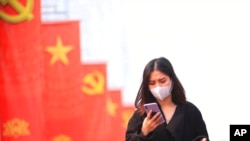FILE - A woman wearing a face mask looks at her phone in Hanoi, Vietnam, Jan. 23, 2021. Vietnam says it has discovered a new coronavirus variant that’s a hybrid of strains first found in India and the U.K. 