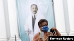 Una mujer sostiene una figura de José Gregorio Hernández mientras caminaba frente a una iglesia en Caracas.
