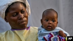 FILE - Two-month-old Lahya Kathembo, whose mother and father died of Ebola, is carried by a nurse waiting for test results at an Ebola treatment center in Beni, DRC, July 17, 2019.