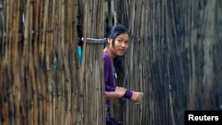 FILE - A refugee who fled Myanmar watches from behind a bamboo wall of a stilt house at Mae La refugee camp, on the Thai side of the Thailand-Myanmar border, July 21, 2014. Many of the 90,000 refugees in nine camps along the border have lived in them for decades.