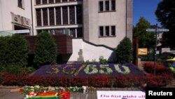 A man writes on a placard near tributes placed on the ground following an incident in which three people were killed by a man who randomly stabbed passers-by with a knife at a city festival in Solingen, Germany, on Aug. 24, 2024.