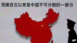 A security guard stands close to an electronic screen featuring a map of China and Chinese characters that read, "Tibet has been an inalienable part of the Chinese territory since ancient times," in Beijing, China, June 28, 2011.