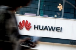 FILE - A woman walks by a Huawei retail store in Beijing, July 30, 2019.
