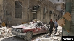People walk near a damaged vehicle after an air strike Sunday in the rebel-held besieged al-Qaterji neighbourhood of Aleppo, Syria October 17, 2016. 