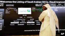 A Saudi stock market official smiles as he watches the stock market screen displaying Saudi Arabia's state-owned oil company in Riyadh, Saudi Arabia, Dec. 11, 2019. 