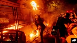 ក្រុម​បាតុករ​គប់​របស់​ដែល​មាន​អណ្ដាត​ភ្លើង​ទៅ​លើ​របង​នៅ​អាគារ​តុលាការ Mark O. Hatfield កាល​ពី​ថ្ងៃ​ទី​២២ កក្កដា ២០២០ នៅ​ទីក្រុង​ Portland រដ្ឋ Orgon។