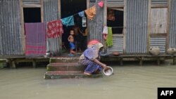 FILE - A woman washes her cooking pot in the flood waters outside her house in Sreenagar on July 20, 2020. (Photo by Munir Uz zaman / AFP)