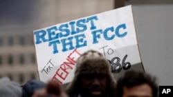 FILE - A protester holds a sign that reads "Resist the FCC. Text: INTERNET To: 52886" at the Federal Communications Commission in Washington, Dec. 14, 2017. 