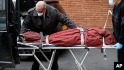 Funeral director Tom Cheeseman, left, and a colleague wear personal protective equipment due to COVID-19 concerns as they deliver a body to a funeral home, April 3, 2020, in the Brooklyn borough of New York.