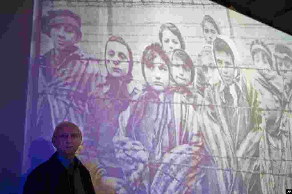 Auschwitz-Birkenau Holocaust survivor Tomy Shacham pose next to a photograph that shows him, on the left, on Jan. 27, 1945, during the International Holocaust Remembrance day ceremony in the Massuah international institute for holocaust studies in Kibbutz.