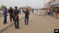 Security officers stand guard at the scene of an explosion at a mobile phone market in Kano, Nigeria. Wednesday Nov. 18, 2015. 