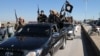 FILE - Islamic State militants pass by a convoy in Tel Abyad town, northeast Syria.