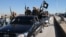 FILE - Islamic State militants pass by a convoy in Tel Abyad town, northeast Syria.