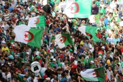 FILE - Demonstrators gesture and carry flags during a protest demanding the removal of the ruling elite and prosecution of former officials linked to former President Abdelaziz Bouteflika, in Algiers, Algeria, June 14, 2019.