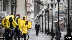 A man walks along pedestrian Arbat street as food delivery couriers talk to each other, in downtown Moscow, April 14, 2020. 