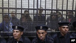 Policemen sit in front of a cage holding Egyptian employees of several pro-democracy groups during court proceedings in Cairo, Egypt, Sunday, February 26, 2012.
