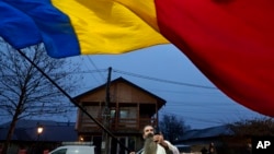 A man waves the Romanian flag outside a voting station after Romania's Constitutional Court annulled the first round of presidential elections, in Mogosoaia, Romania, Dec. 8, 2024. 
