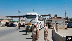 This photo released by the Syrian official news agency SANA, shows Syrian government forces overseeing the evacuation by bus of Army of Islam fighters from the besieged town of Douma, just east of Damascus, Syria, Apr. 2, 2018. 