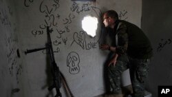 Macer Gifford, a 30-year former City broker in London, who fights with an Assyrian militia, that is part of the U.S-backed forces battling Islamic State group militants, looks through a hole into a street controlled by the IS, on the western side of Raqqa, northeast Syria, July 17, 2017.