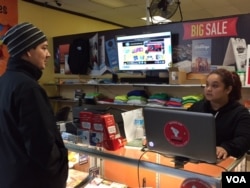Marcela Bedoya, behind the counter, owns Print and Save in Indianapolis, Indiana, with her husband. Luis Bustos, who is from Mexico City, Mexico. (C. Presutti/VOA)