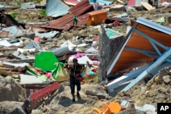 A man carry items he saved from the rubble following a major earthquake and tsunami in Palu, Central Sulawesi, Indonesia, Monday, Oct. 1, 2018.