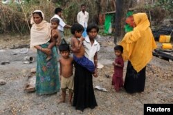 FILE - A family stands beside remains of a market which was set on fire, in a Rohingya village outside Maungdaw, in Rakhine state, Myanmar, Oct. 27, 2016.