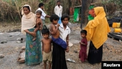 A family stands beside remains of a market which was set on fire, in Rohingya village outside Maungdaw, in Rakhine state, Myanmar, Oct. 27, 2016. 
