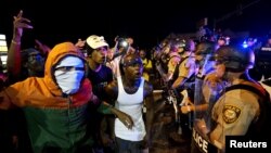 Para pengunjuk rasa meneriakkan protes ke arah barisan polisi sebelum terjadinya penembakan di Ferguson, Missouri (9/8). 