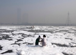 A woman bathes her daughter in the Yamuna River, covered by a chemical foam caused by industrial and domestic pollution as the skyline is enveloped in toxic smog, in New Delhi, India, Nov. 17, 2021.