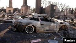 A sign sits on the ground next to a car destroyed by the Palisades Fire, in the Pacific Palisades neighborhood in Los Angeles, Jan. 14, 2025.