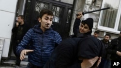A civilian, left, and a security officer beat a protester as riot police use water cannons to disperse people protesting the detentions of 12 lawmakers from pro-Kurdish Peoples' Democratic Party, or HDP, in Istanbul, Nov. 5, 2016.