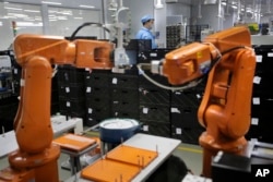 FILE - A Chinese worker is seen behind orange robot arms at Rapoo Technology factory in the southern Chinese industrial boomtown of Shenzhen, Aug. 21, 2015. Automation could wipe out two thirds of jobs in some countries, the World Bank warns.