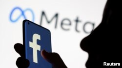 FILE - A woman holds a smartphone with the Facebook logo in front of a display of Facebook's new rebrand logo Meta in this illustration picture taken October 28, 2021.