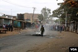 A Kenyan police officer tries to put out flames from a burning tire in Nairobi’s Kibera slum, Aug. 12, 2017. (J. Craig/VOA)