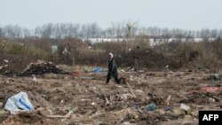 FILE - A man walks among remains of taken down shelters during the dismantling of the southern part of the so-called "Jungle" migrant camp in Calais, northern France, March 10, 2016.