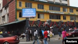 Pedestrians walk past a sign reading "Ebola disease outbreak" outside the Ministry of Finance in Monrovia, Liberia, Jan. 12, 2015.