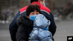 A Chinese families wearing masks ride on a tricycle on a street in Beijing, Feb. 8, 2020.