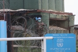 FILE - A peacekeeper of the United Nations Interim Force in Lebanon (UNIFIL), wearing gloves and a protective face mask, gestures from his post in the village of Markaba, during a countrywide coronavirus lockdown, in southern Lebanon, April 17, 2020.