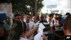 Migrants listen as a Mexican migration officer verifies their identity from a list in Matamoros, Mexico, at the foot of the Puerta Mexico bridge that crosses into Brownsville, Texas, Aug. 2, 2019.