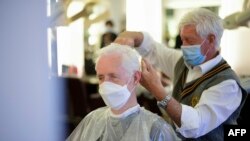 FILE - A barber wearing a face mask cuts the hair of a client, also masked, at his barber shop in Dortmund, Germany, May 4, 2020, amid signs of the coronavirus spread slowing in the country. 